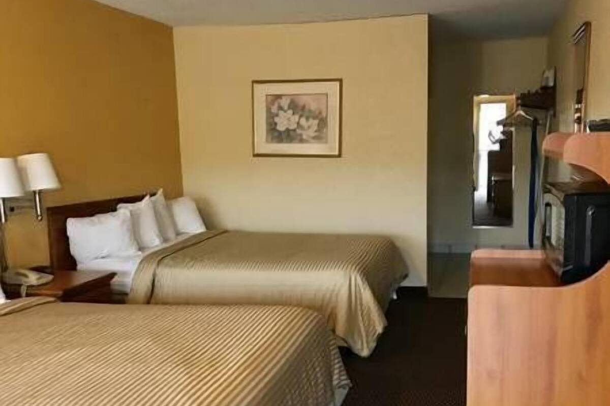 A hotel room with two beds, a wooden desk, a lamp, and a framed picture on the wall.