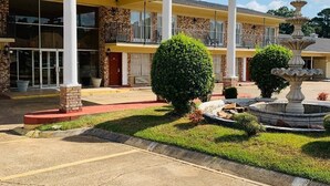 A building with a covered entrance, a fountain, and a well-maintained lawn. - Coachman's Inn (Magnolia)