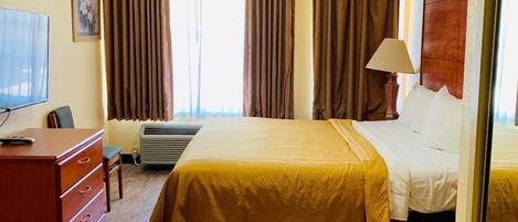 A hotel room with a bed, a desk with a chair, a television, and a window with curtains.