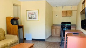 A compact living space with a sofa, a small table, a kitchenette with a stove and microwave, and a television. - Coachman's Inn (Magnolia)