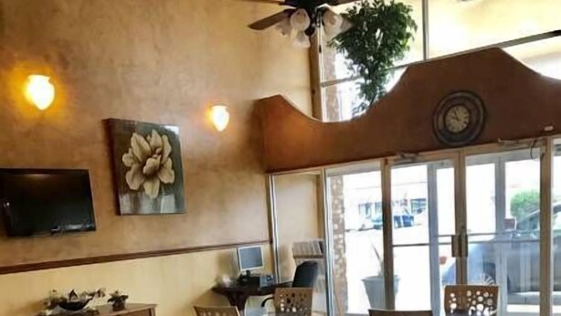 A restaurant interior with tables and chairs, a ceiling fan, a clock, and a TV on the wall. - Coachman's Inn (Magnolia)
