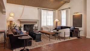 Un salon spacieux doté d’une cheminée, de nombreux sièges et d’une grande fenêtre agrémentée de rideaux.