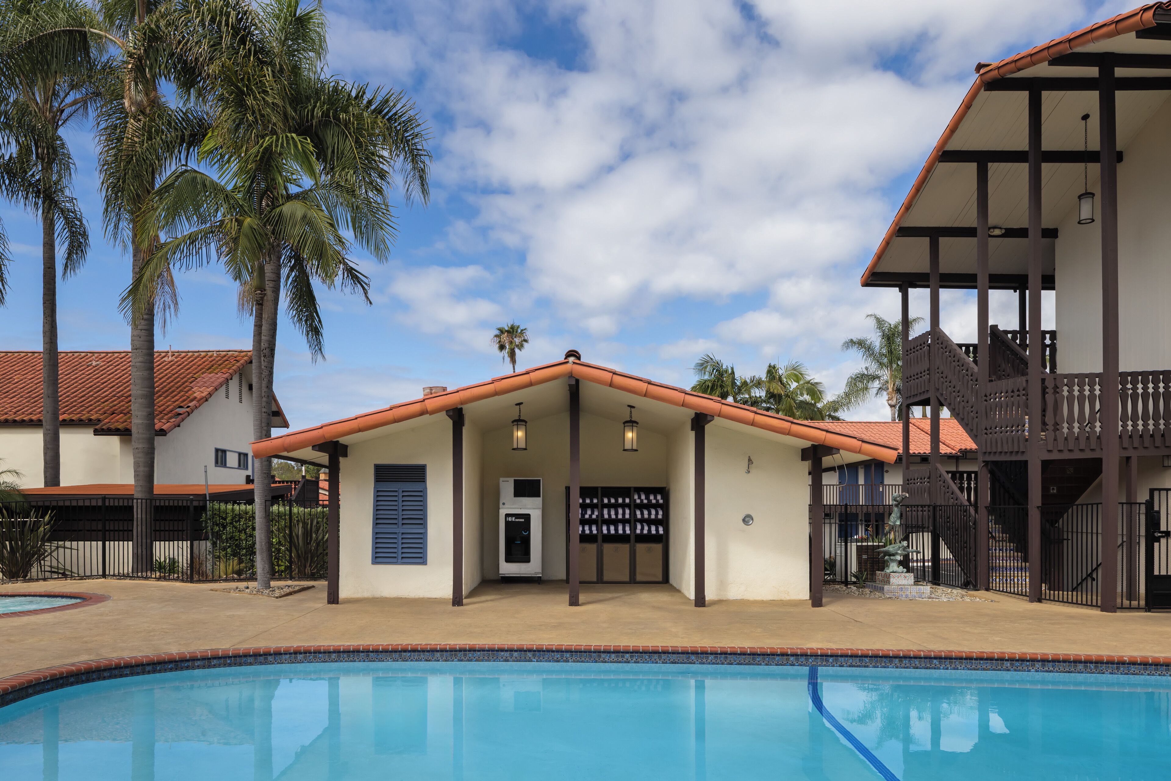 A poolside area with a building that has a covered patio, a water fountain, and a vending machine.