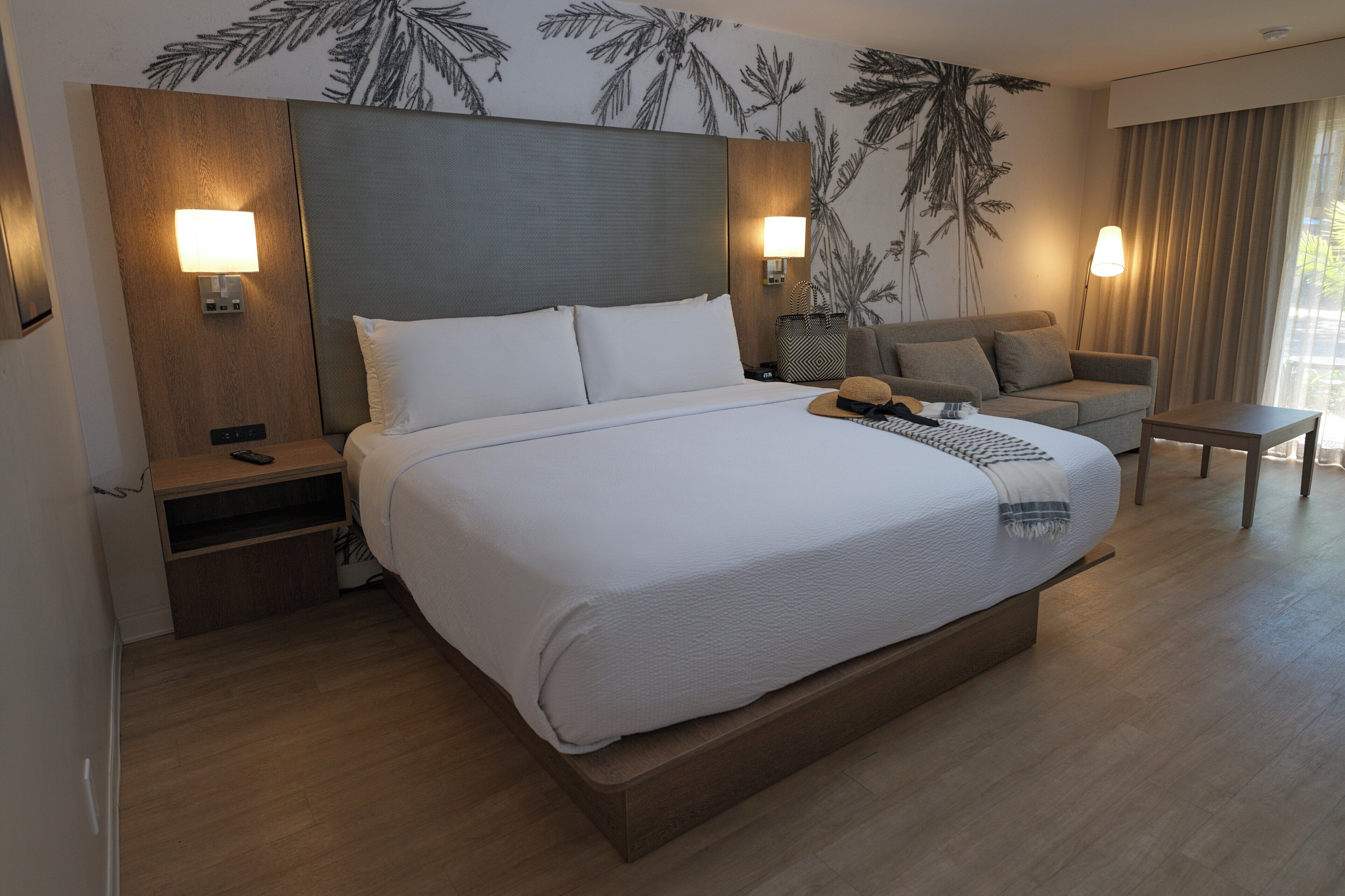 Une chambre d’hôtel avec un grand lit, une table de chevet, une commode, un canapé, une petite table et une lampe.