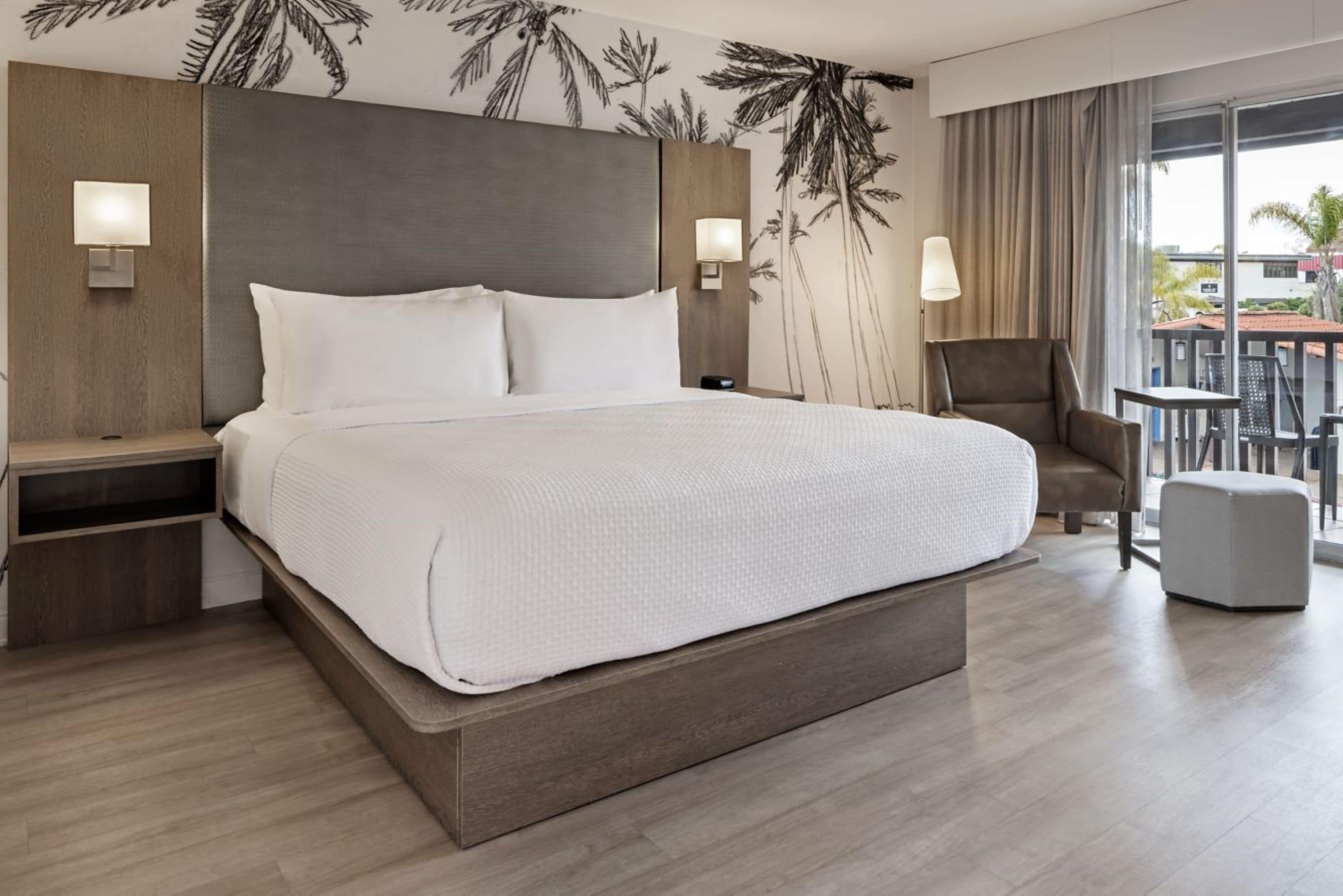 A hotel room with a large bed, two bedside tables, a chair, and a view of the outdoors.