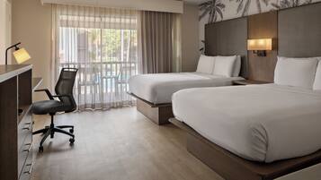 Une chambre d’hôtel avec deux lits, un bureau, une chaise, une lampe et une vue sur l’extérieur, visible à travers une fenêtre avec des rideaux.