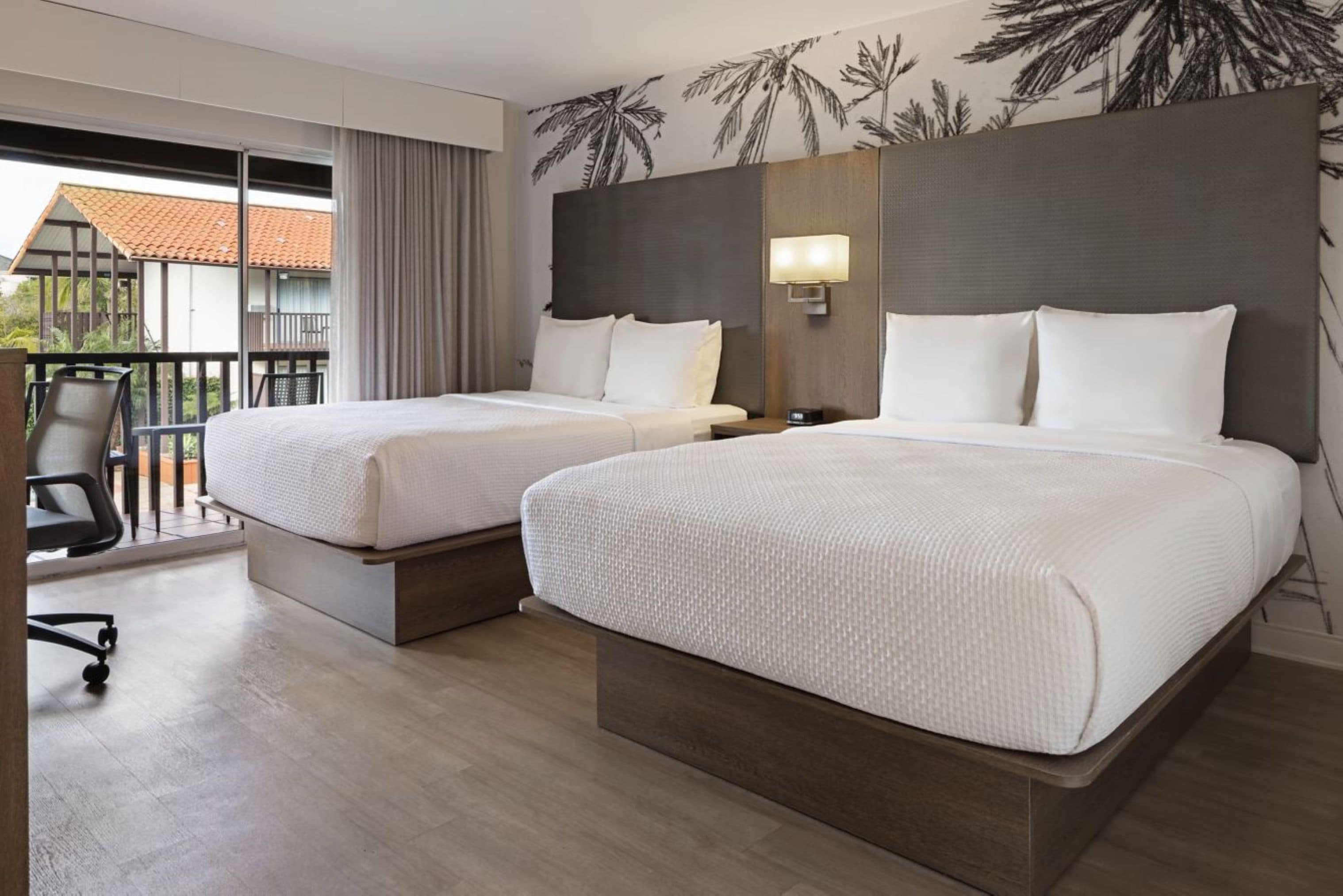 Habitación de hotel con dos camas, un balcón y vistas al exterior.