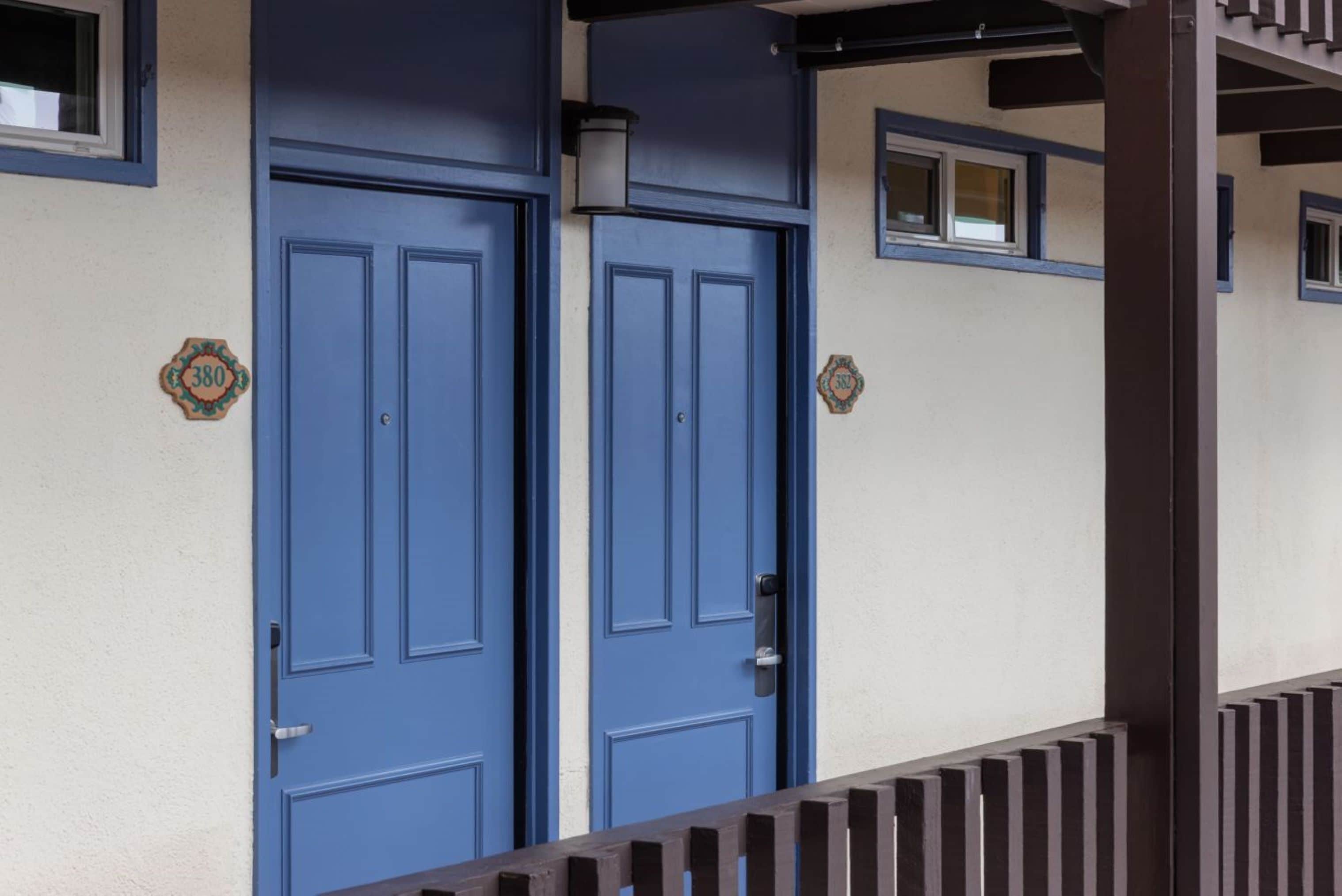Un bâtiment avec deux portes bleues, une petite fenêtre et une balustrade en bois.