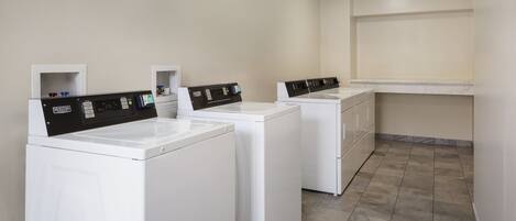 A laundry area with three white washing machines, a countertop, and a tiled floor.