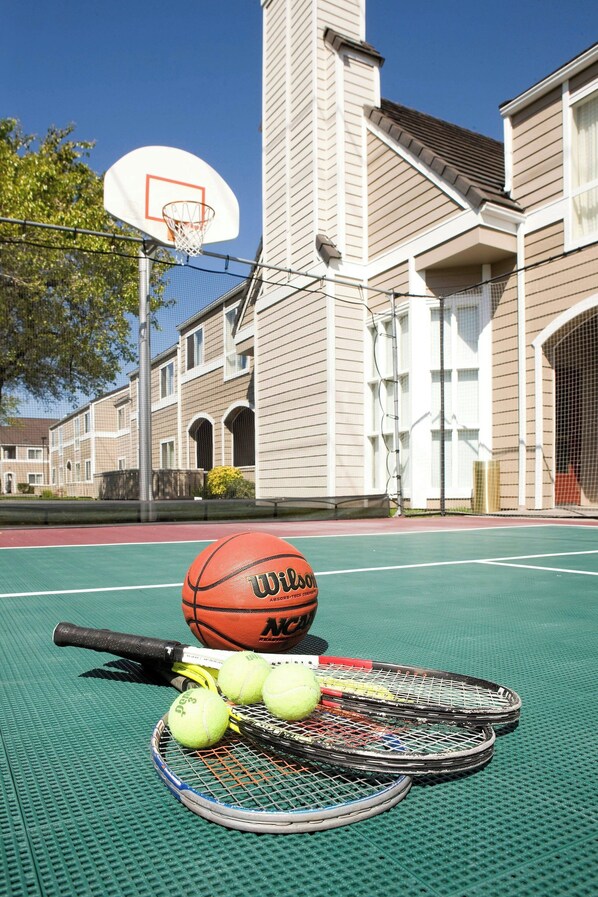 Uma quadra de basquete com uma cesta, raquetes de tênis e bolas de tênis.
