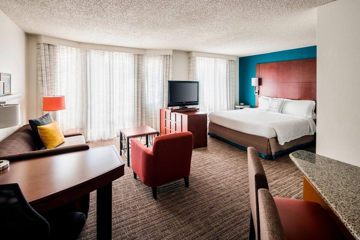 A hotel room with a bed, a TV, a desk, a chair, and a sofa.