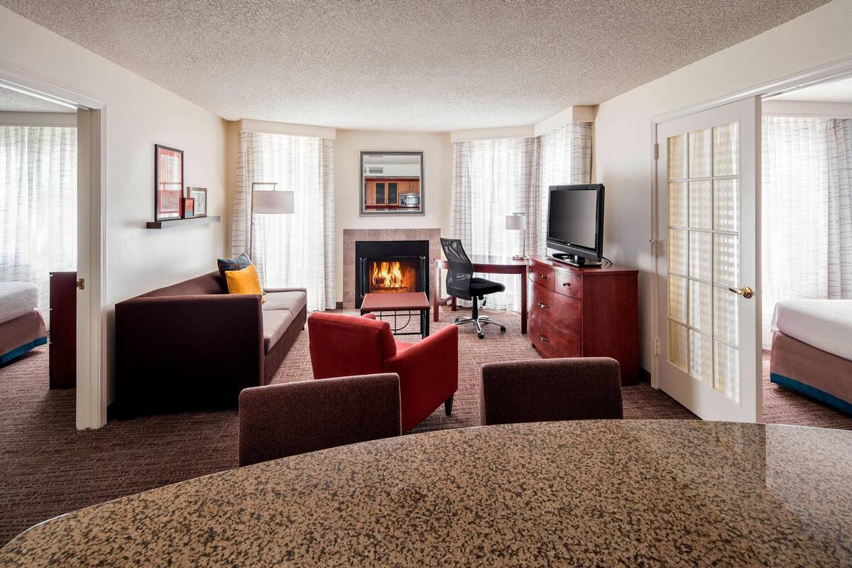 A hotel room with a fireplace, a TV, a dining table, and a sofa.