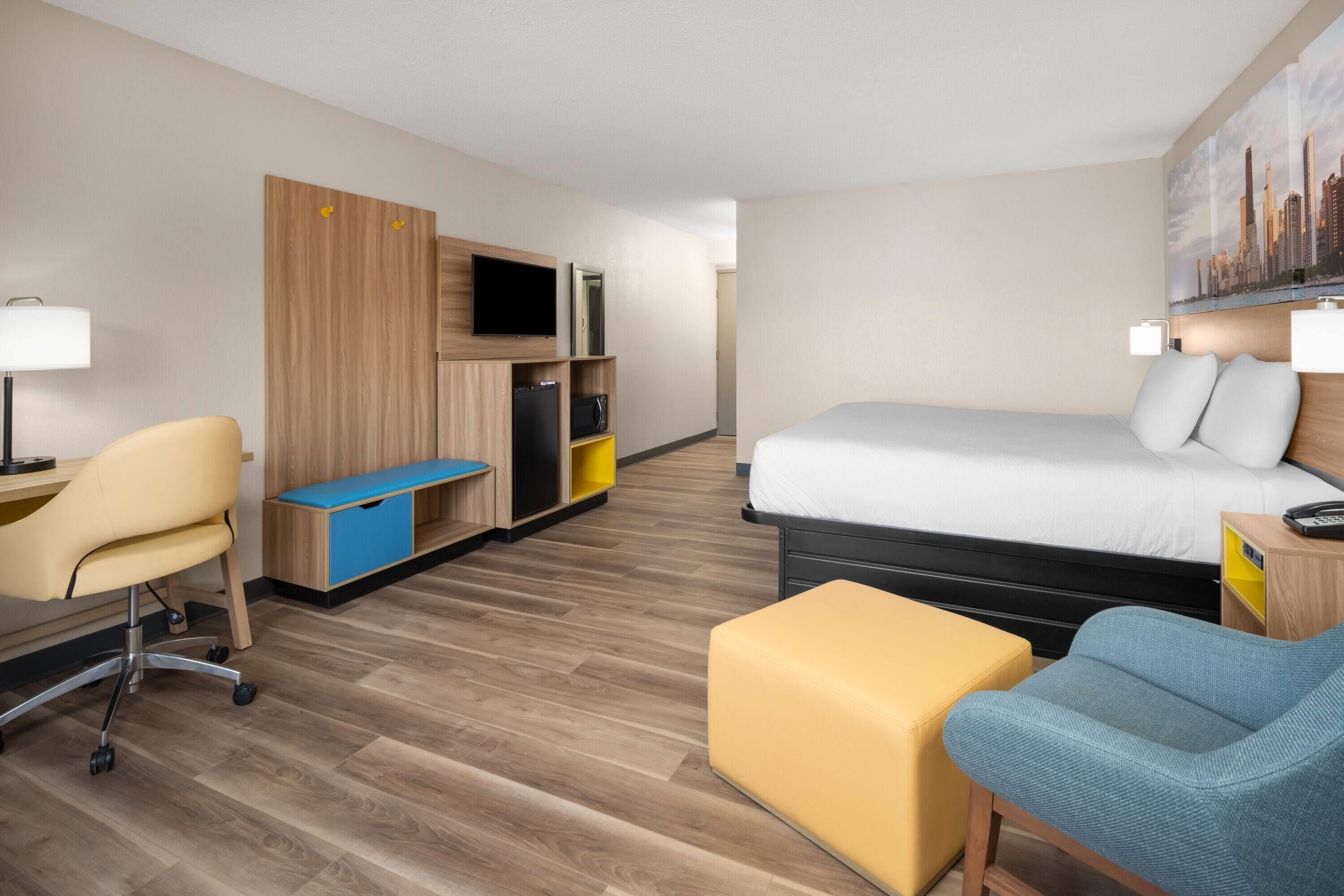 Ett hotellrum med en säng, ett skrivbord med en stol, en soffa, en tv och en tavla på väggen.