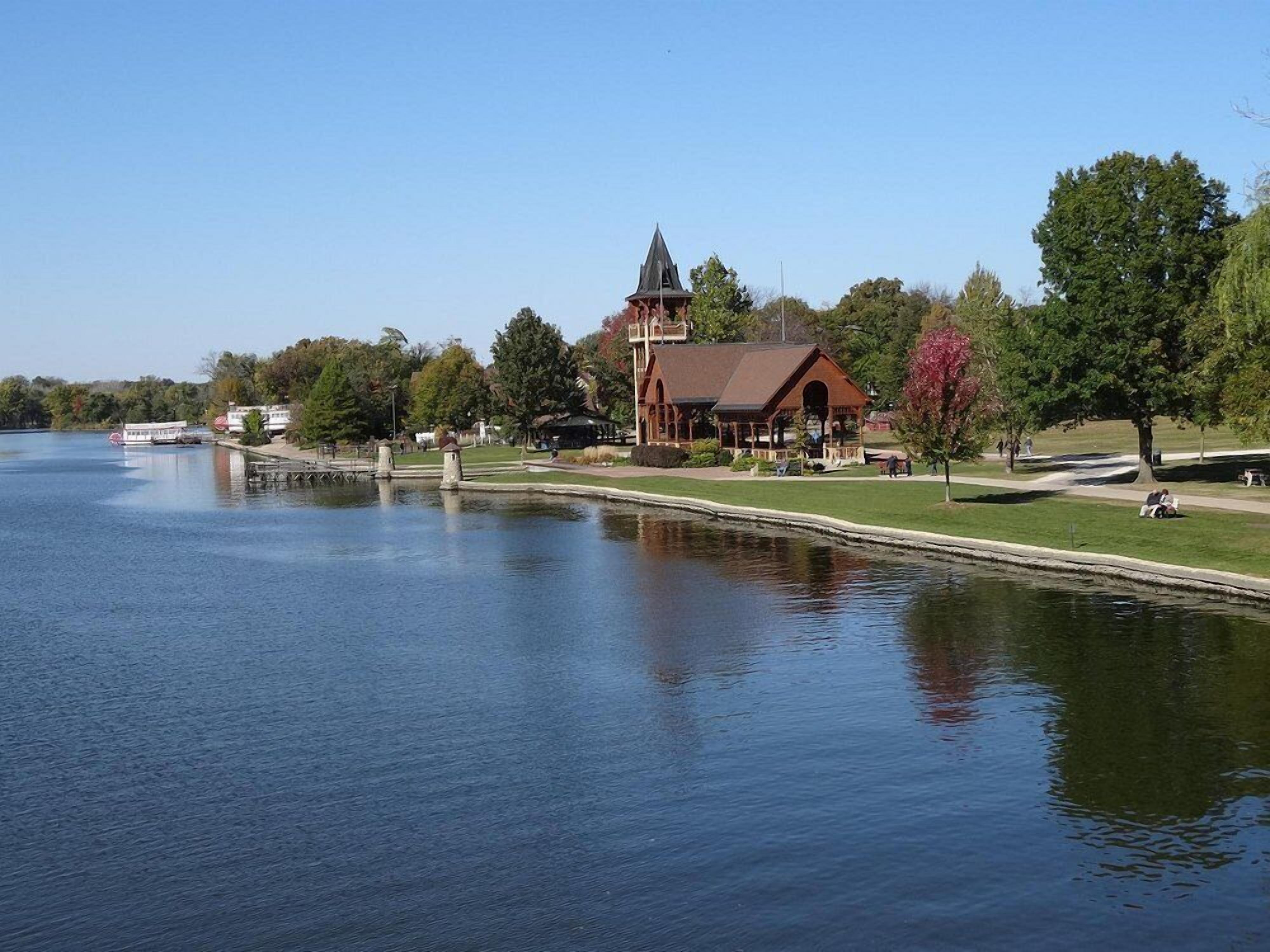 A lakeside building with a prominent tower, surrounded by trees and a grassy area.
