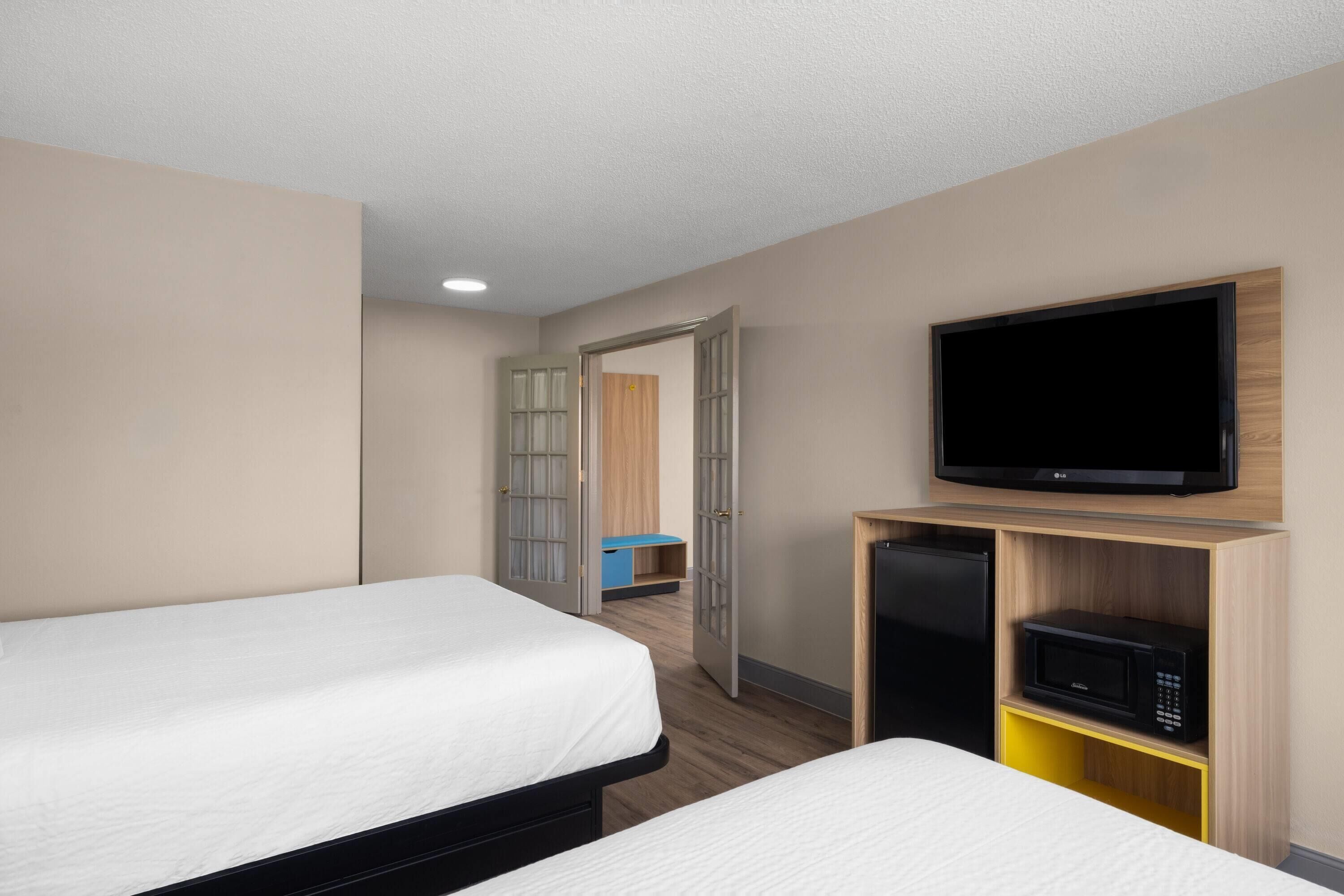 A hotel room with two beds, a television, a microwave, and a door leading to a bathroom.