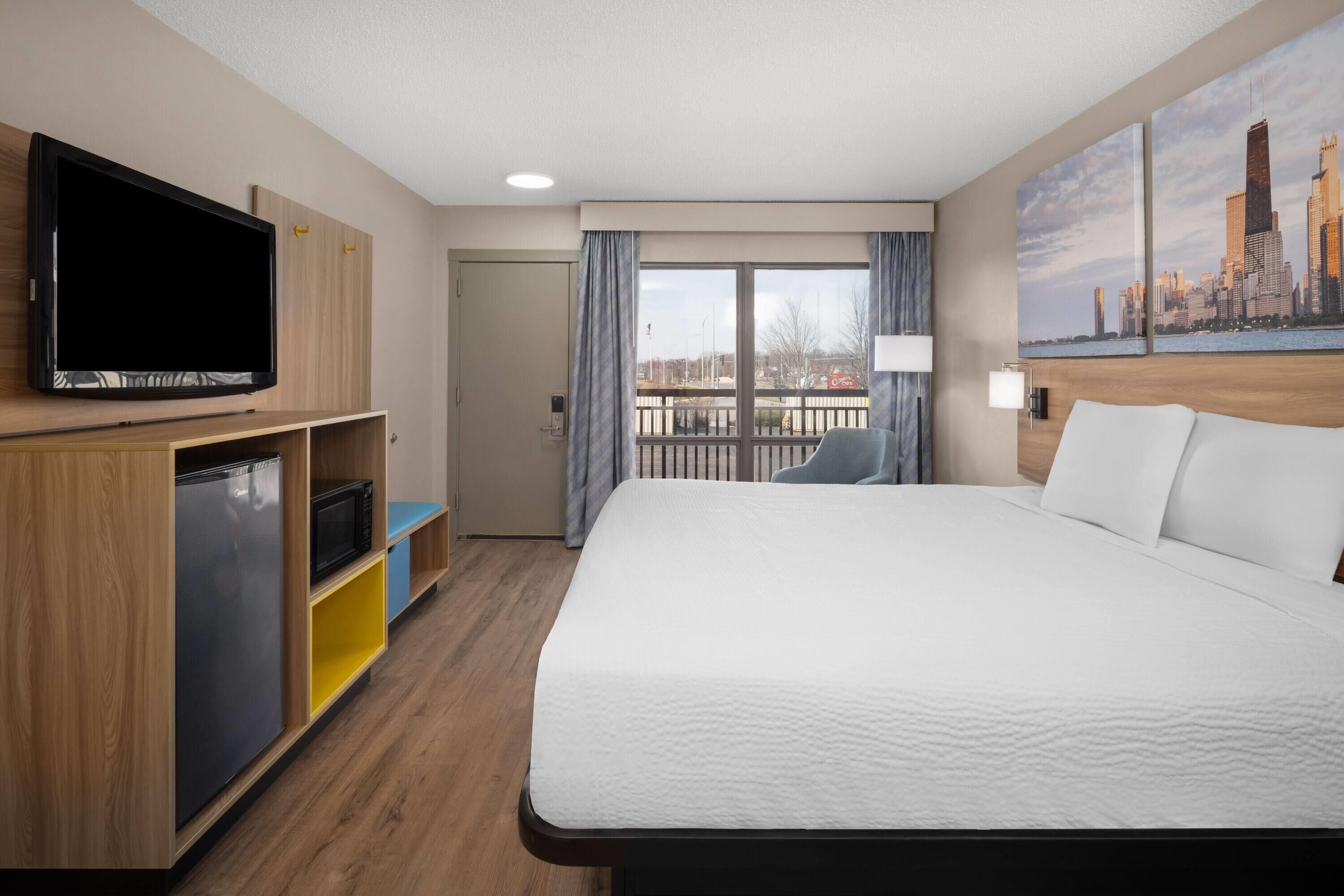 Ein Hotelzimmer mit Bett, Fernseher, Minibar, Schreibtisch und einem Balkon mit Blick auf die Stadt.
