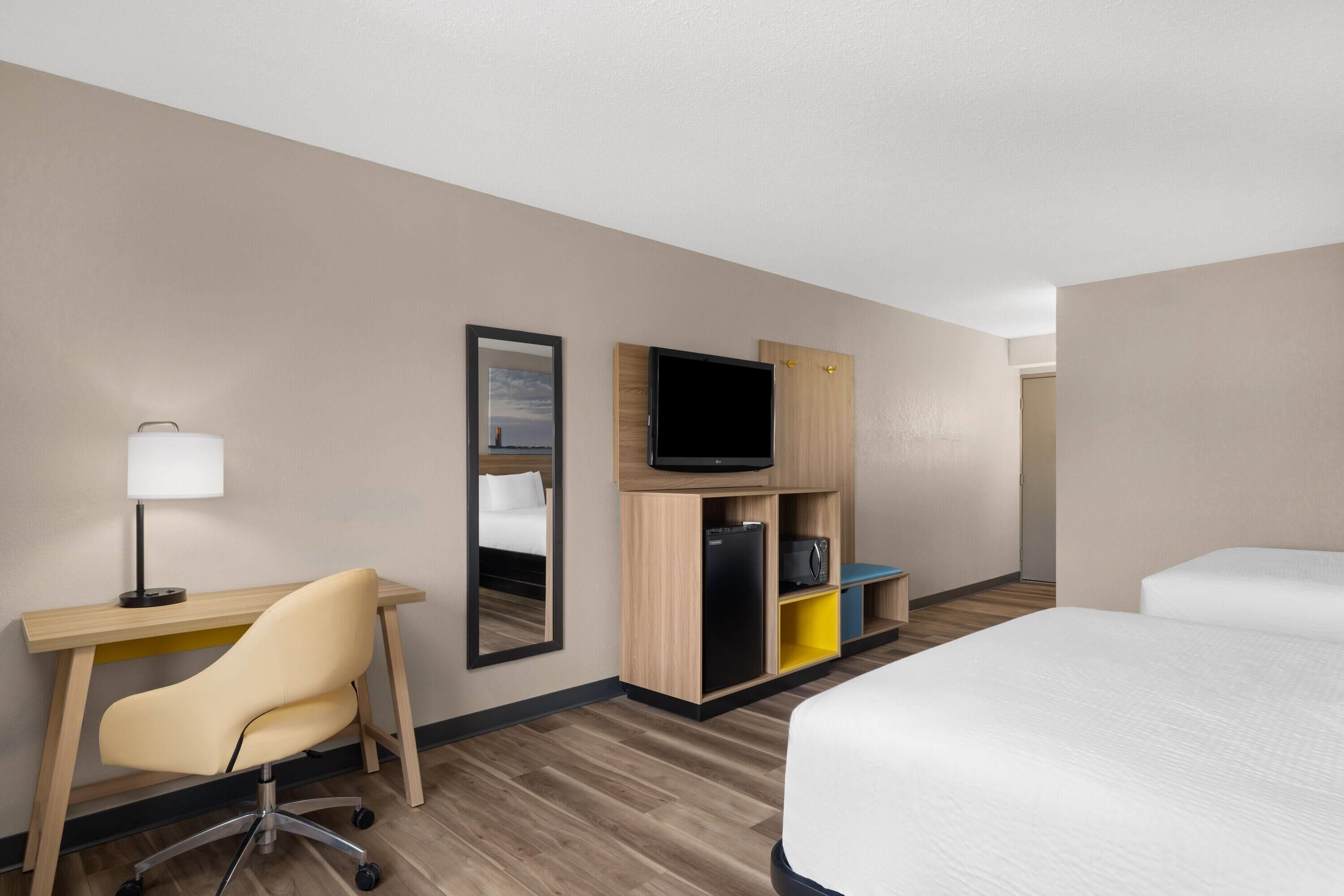 Una habitación de hotel con escritorio, silla, televisor, armario y cama.