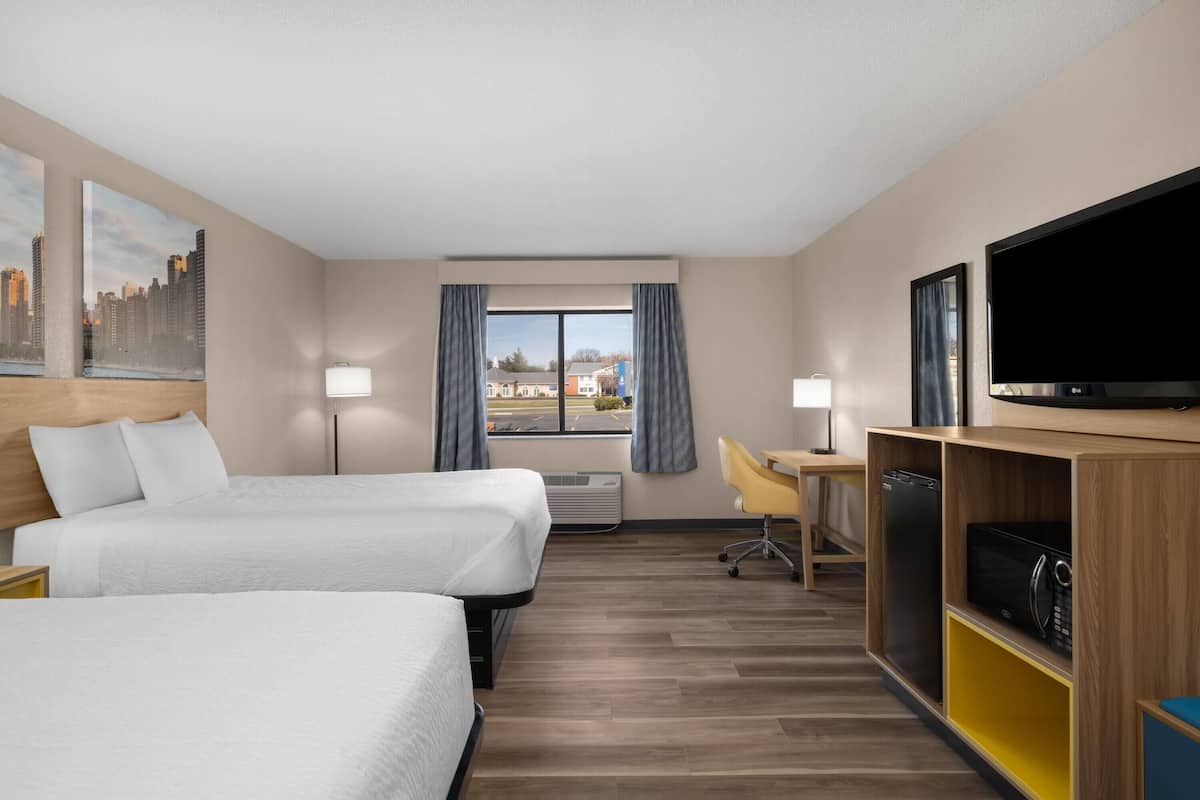 A hotel room with two beds, a desk, a TV, and a view of the city.
