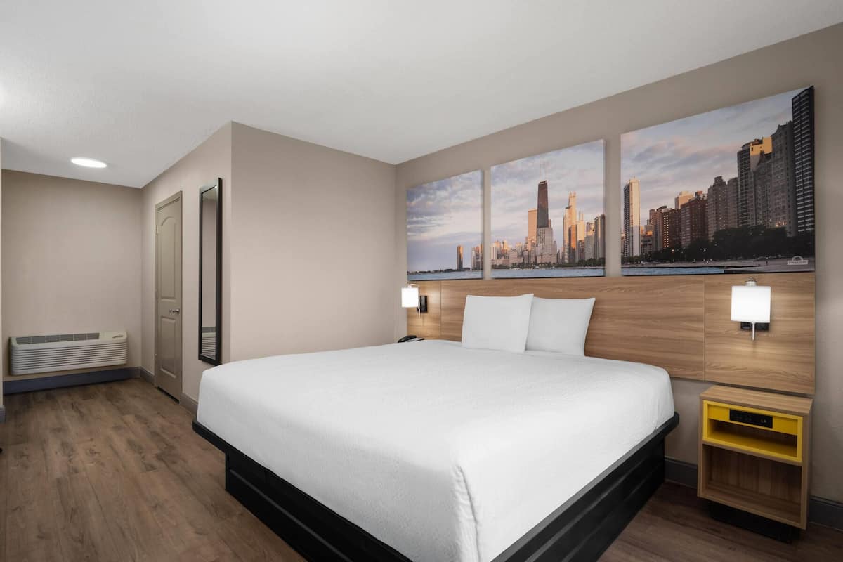 A hotel room with a large bed, a cityscape view, a wooden headboard, and a nightstand with a lamp.