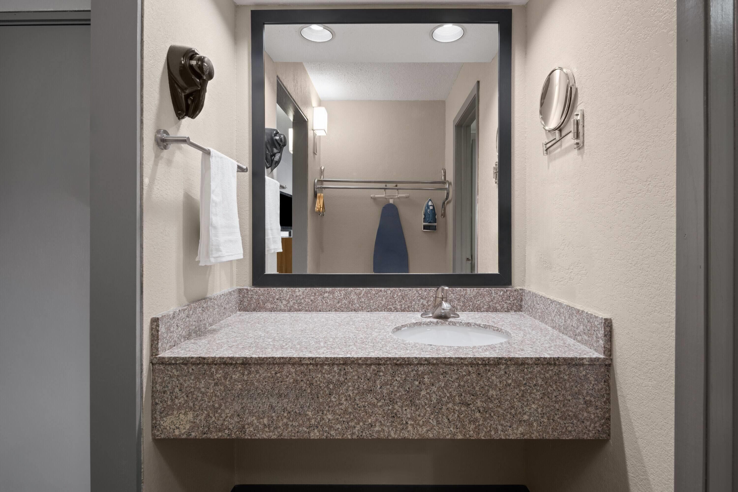 A bathroom with a granite countertop sink, a mirror, a towel rack, and a shower area visible in the reflection.
