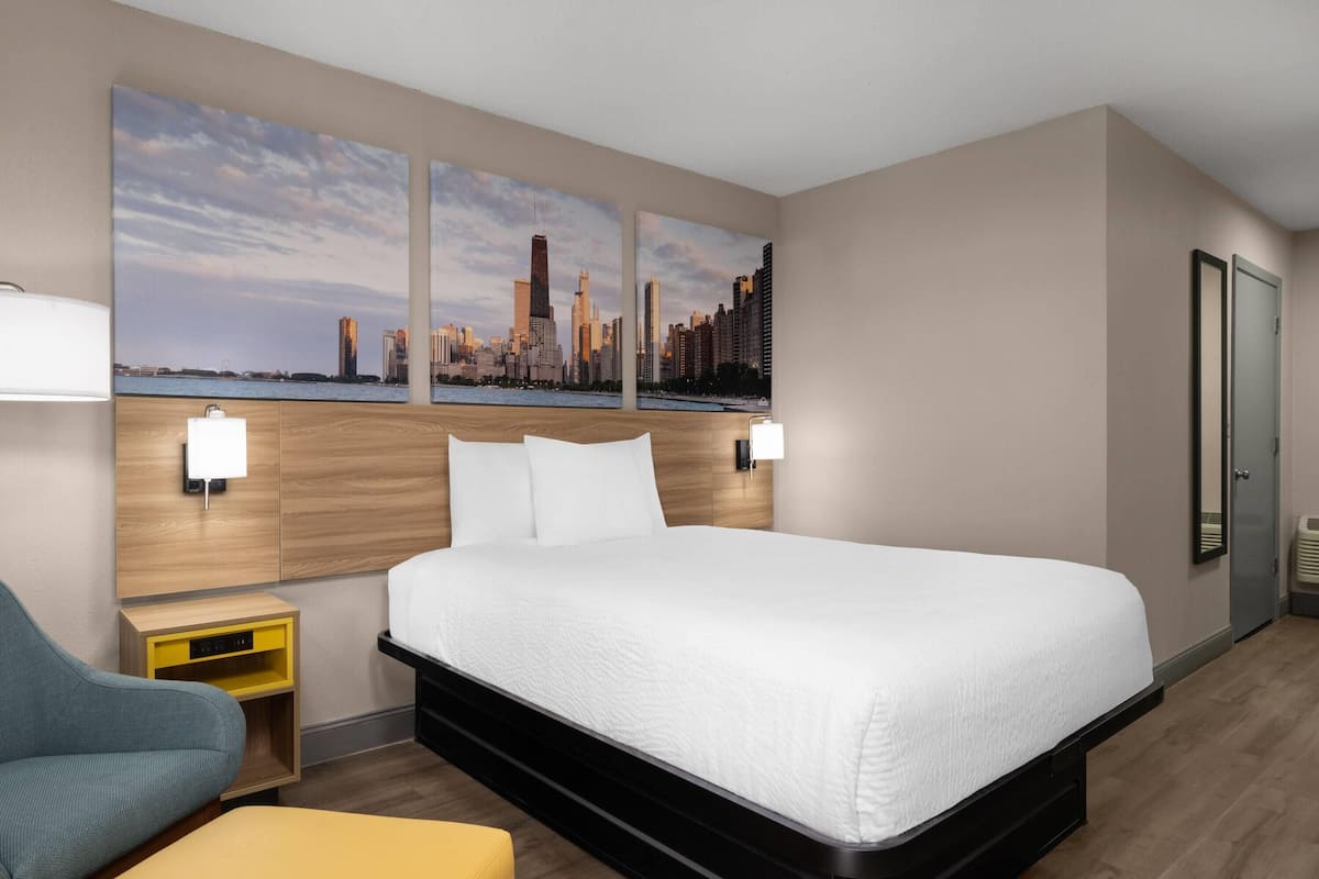 A hotel room with a large bed, a desk, a chair, a nightstand, and two wall-mounted lamps.