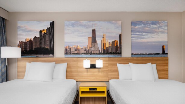 A hotel room with two beds, a wooden headboard, a cityscape view, and a nightstand with a yellow drawer. - Days Inn by Wyndham St. Charles IL (St. Charles)