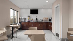A modern kitchen with a flat-screen TV, wooden cabinets, and a dining area with a table and chairs. - Days Inn by Wyndham St. Charles IL (St. Charles)