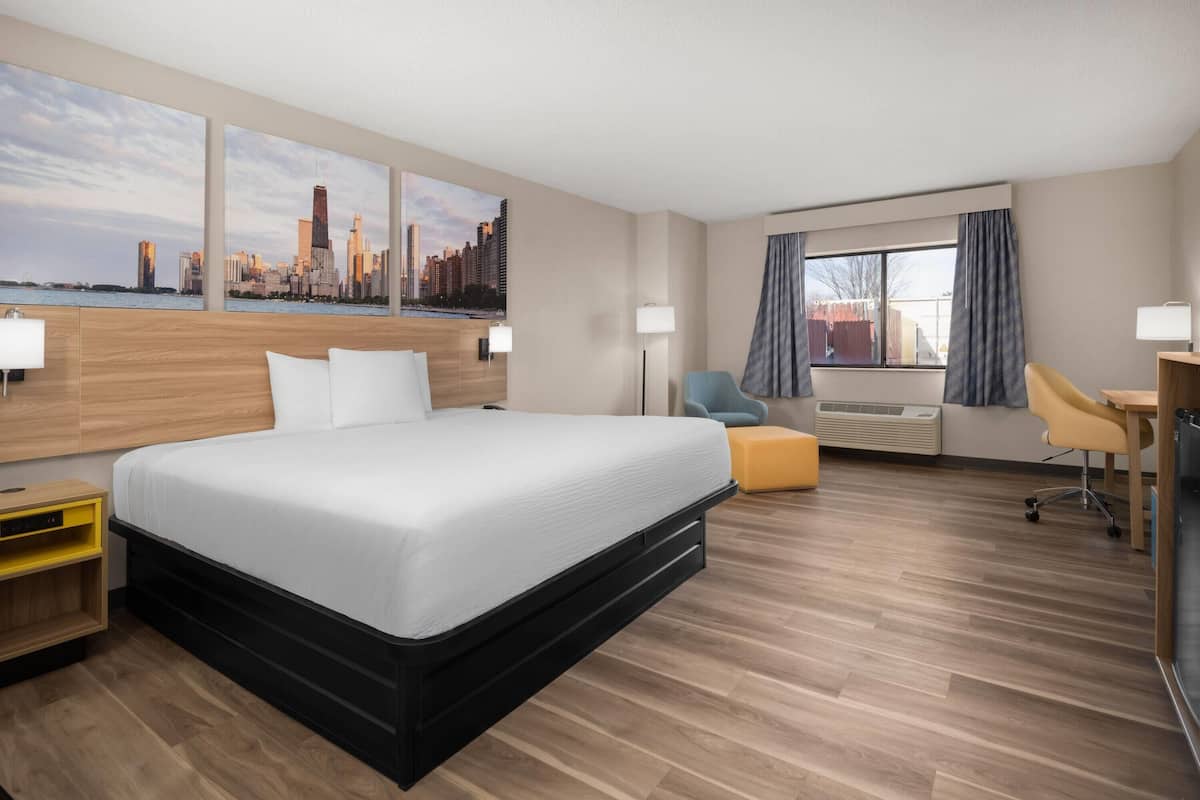 A hotel room with a large bed, a desk, a chair, a sofa, and a window with curtains.