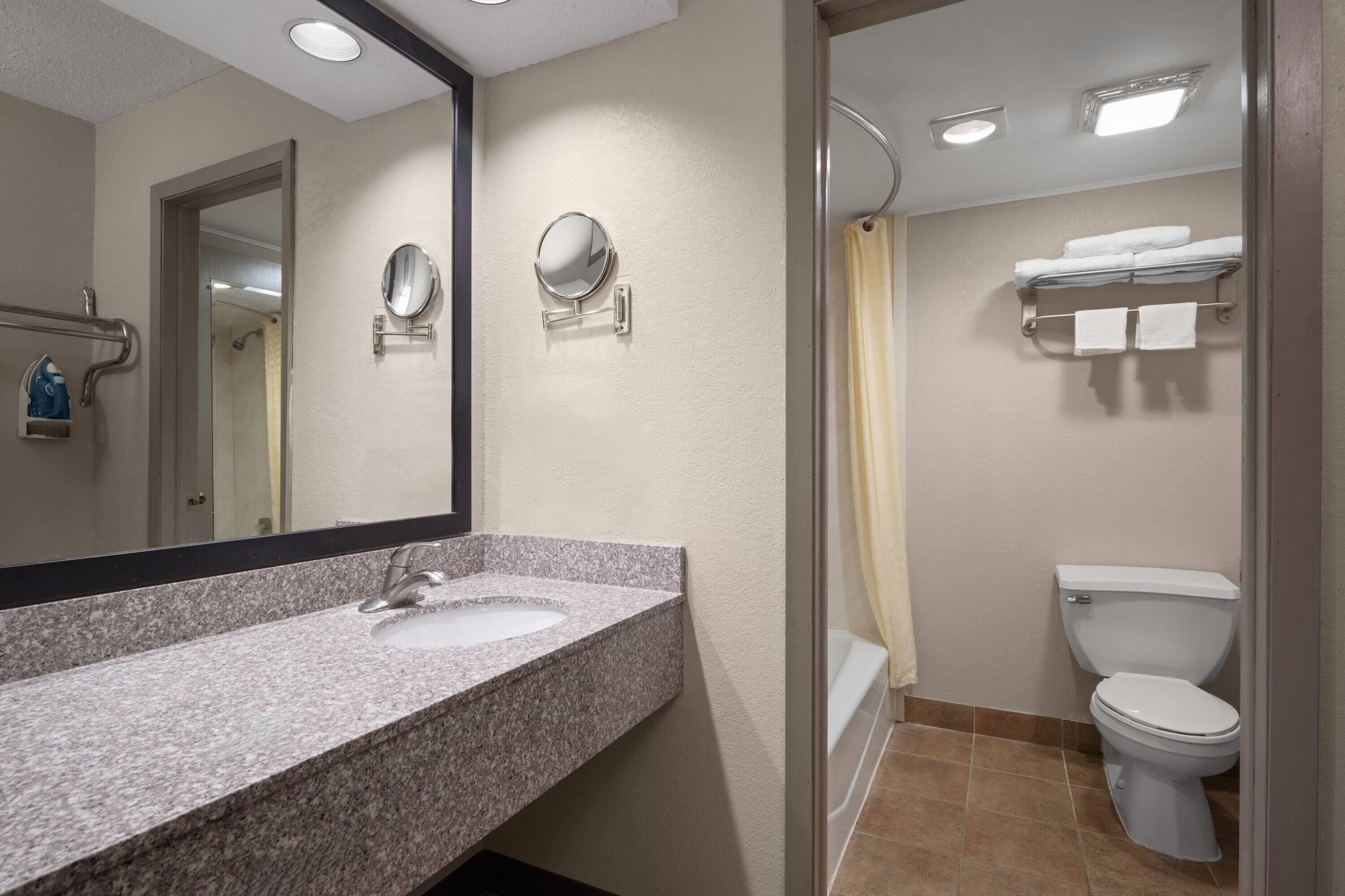 A bathroom with a granite sink, two wall-mounted mirrors, a toilet, and a shower curtain.