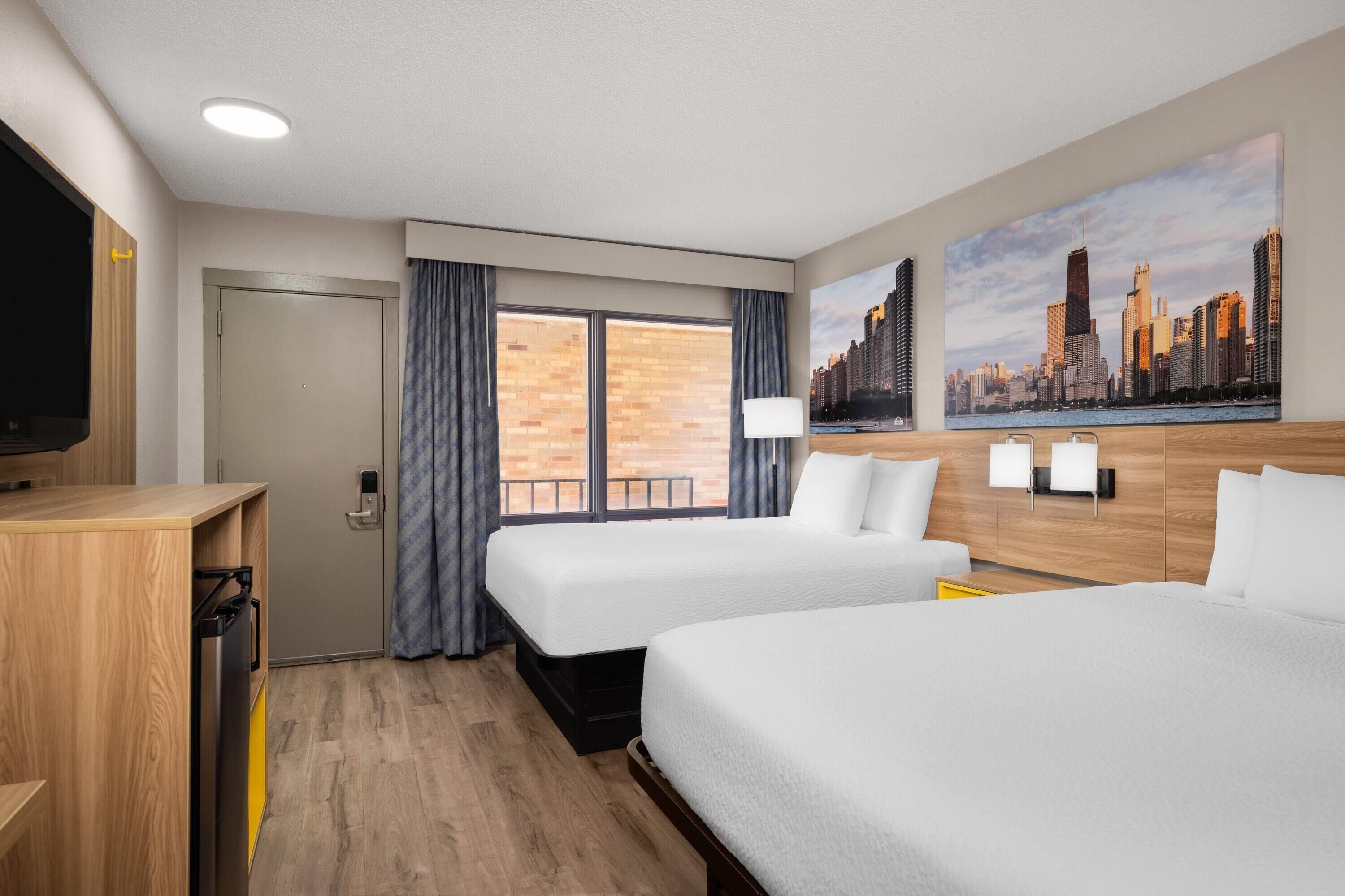 A hotel room with two beds, a TV, a cityscape painting, and a window with curtains.
