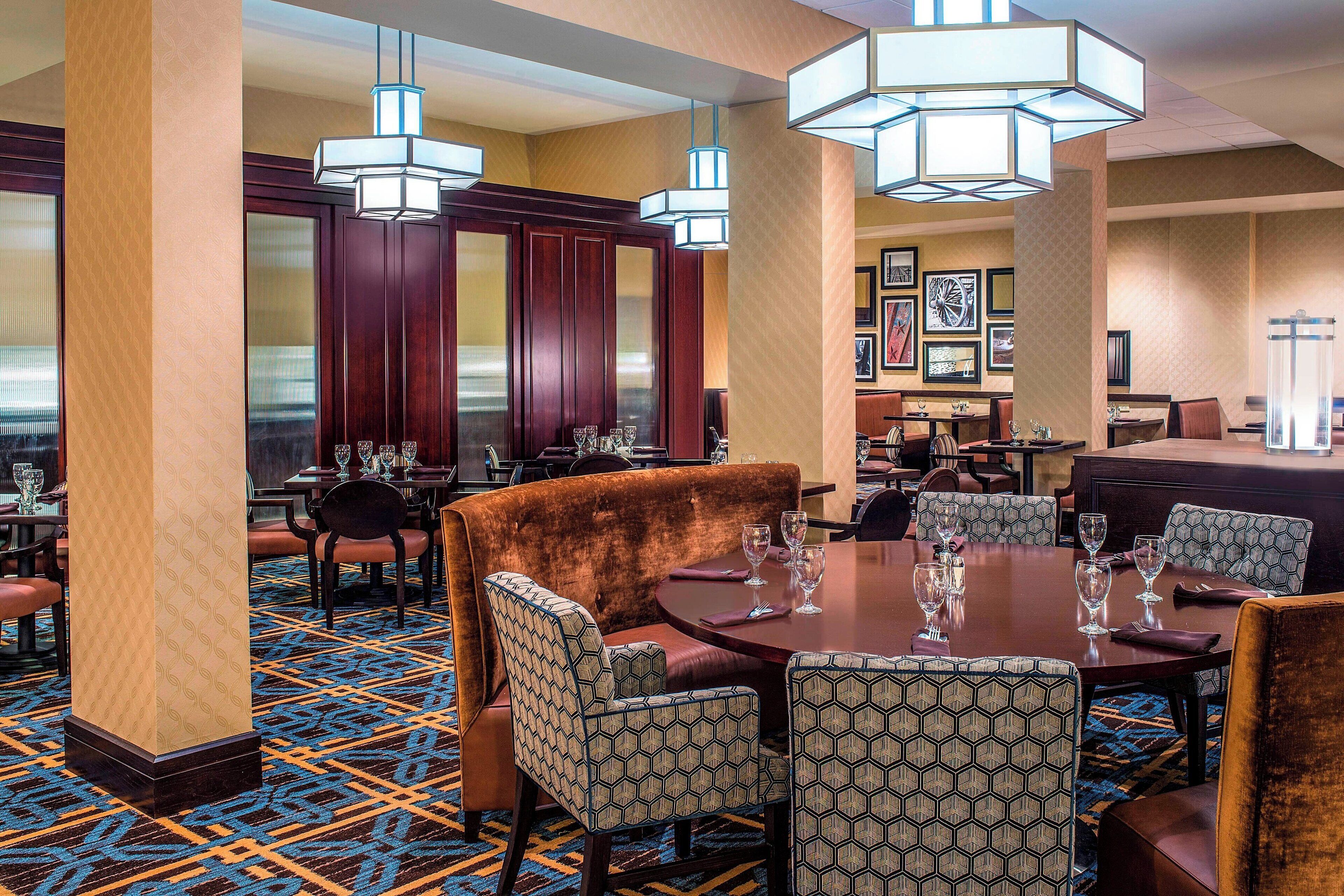 Un comedor de hotel con alfombra estampada, mobiliario de madera e iluminación colgante.