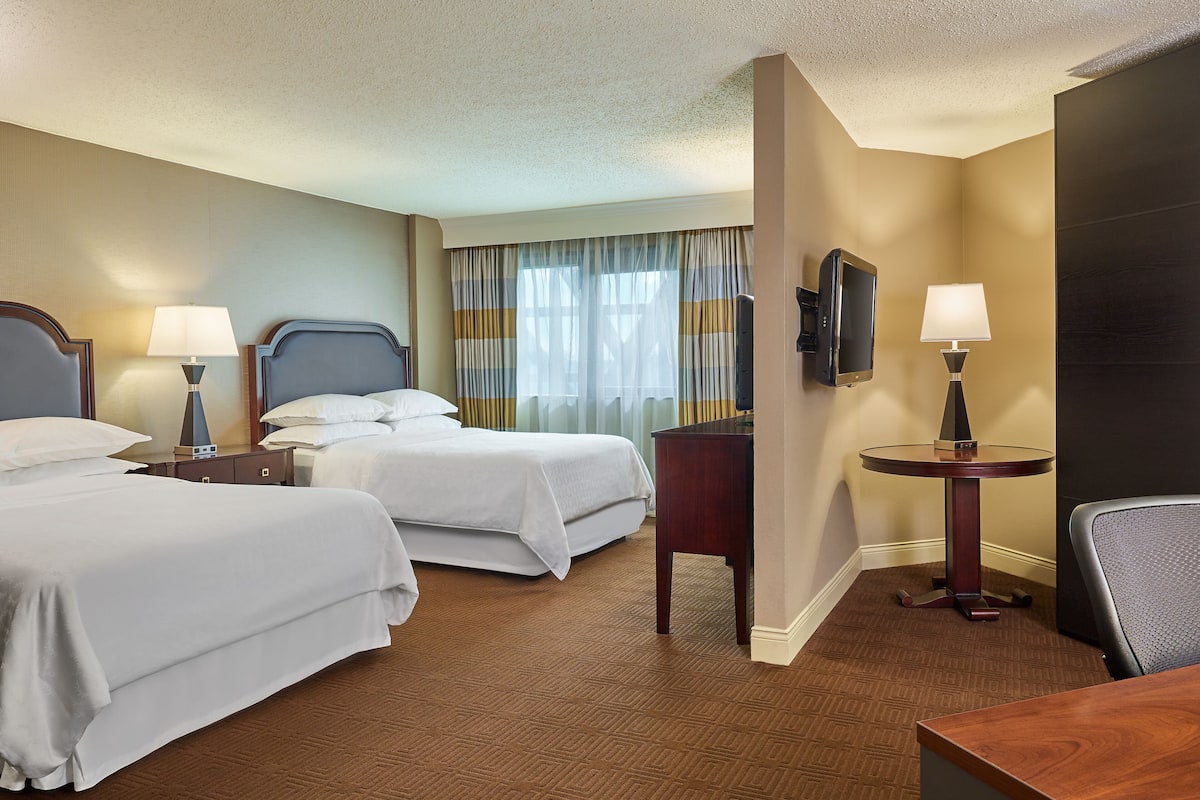 A hotel room with two beds, a desk, a chair, a TV, and a window with curtains.