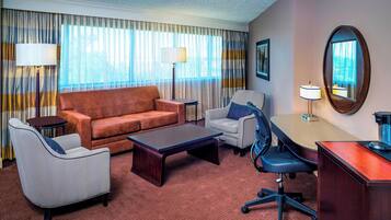 A hotel room with a sofa, armchair, desk, and chairs.