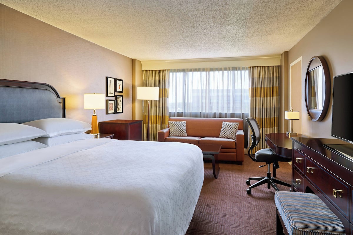 A hotel room with a large bed, a sofa, a desk, a chair, and a television.