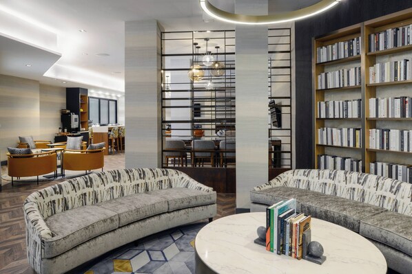A modern library with curved sofas, a marble coffee table, and bookshelves filled with books.
