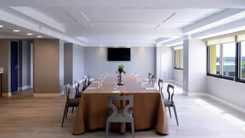 Un salón de conferencias con una mesa larga, sillas, una televisión de pantalla plana y ventanas amplias.