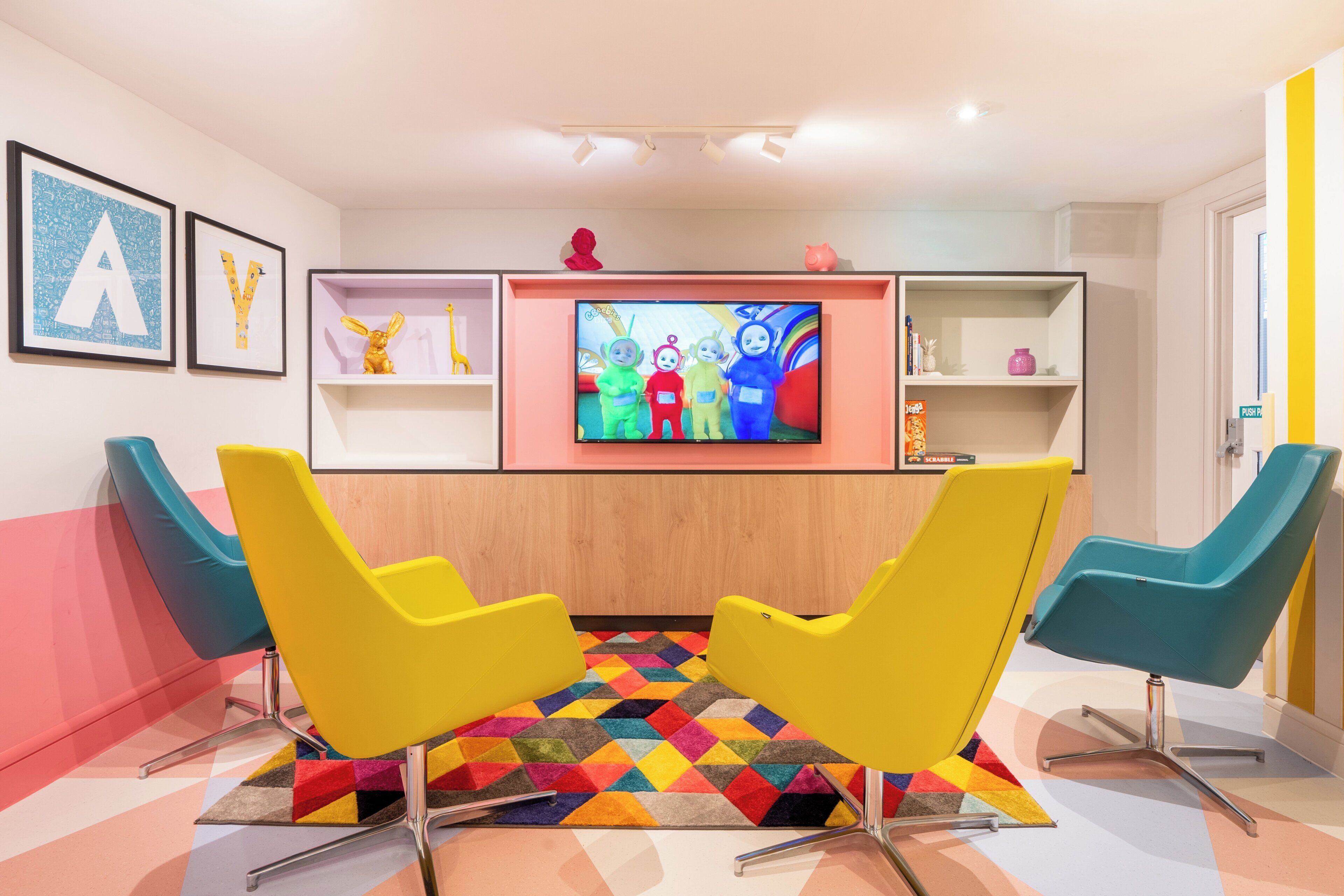 A modern living room with two yellow chairs, a colorful rug, a TV on the wall, and framed artwork.