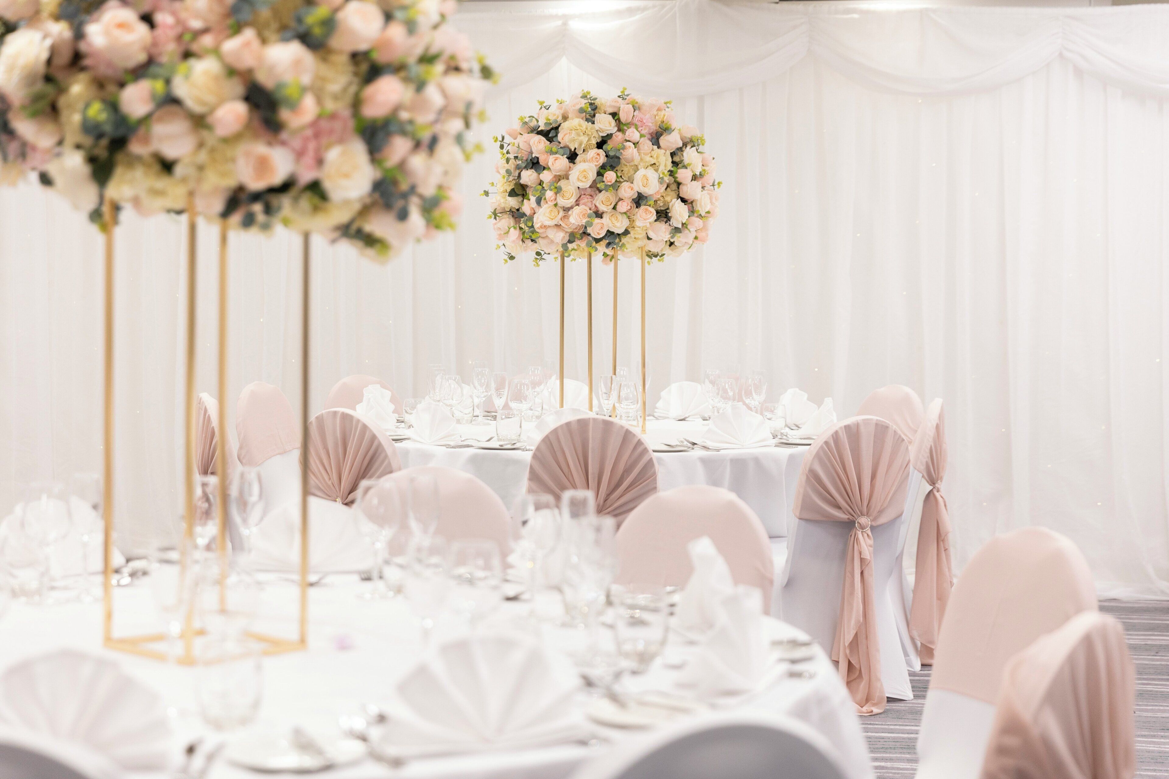 A banquet hall with round tables set for a formal event, featuring white tablecloths and chairs with light-colored sashes.
