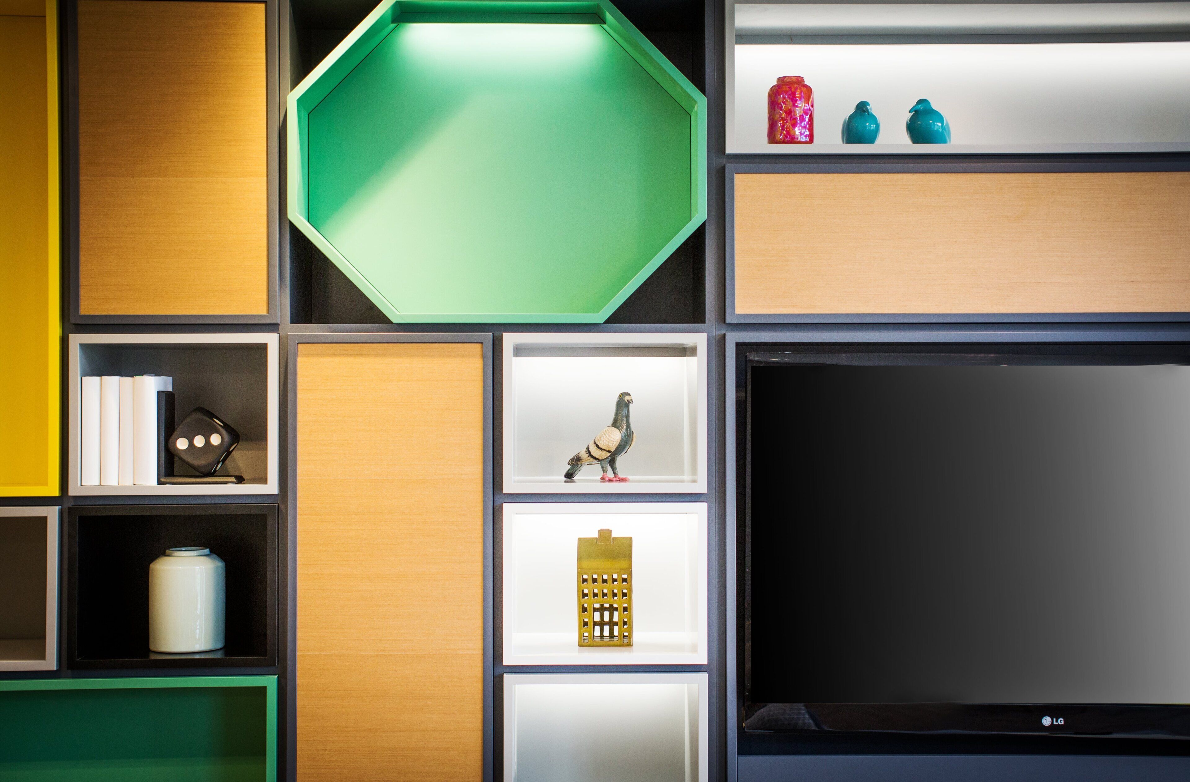 Un interno moderno con una TV a schermo piatto, diverse mensole con oggetti decorativi e una parete verde a contrasto.