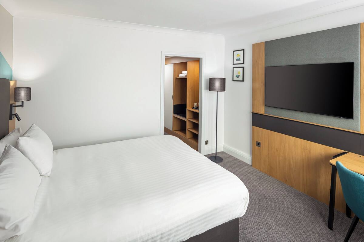 Une chambre d’hôtel avec un grand lit, un bureau, une télévision, une armoire et une lampe.