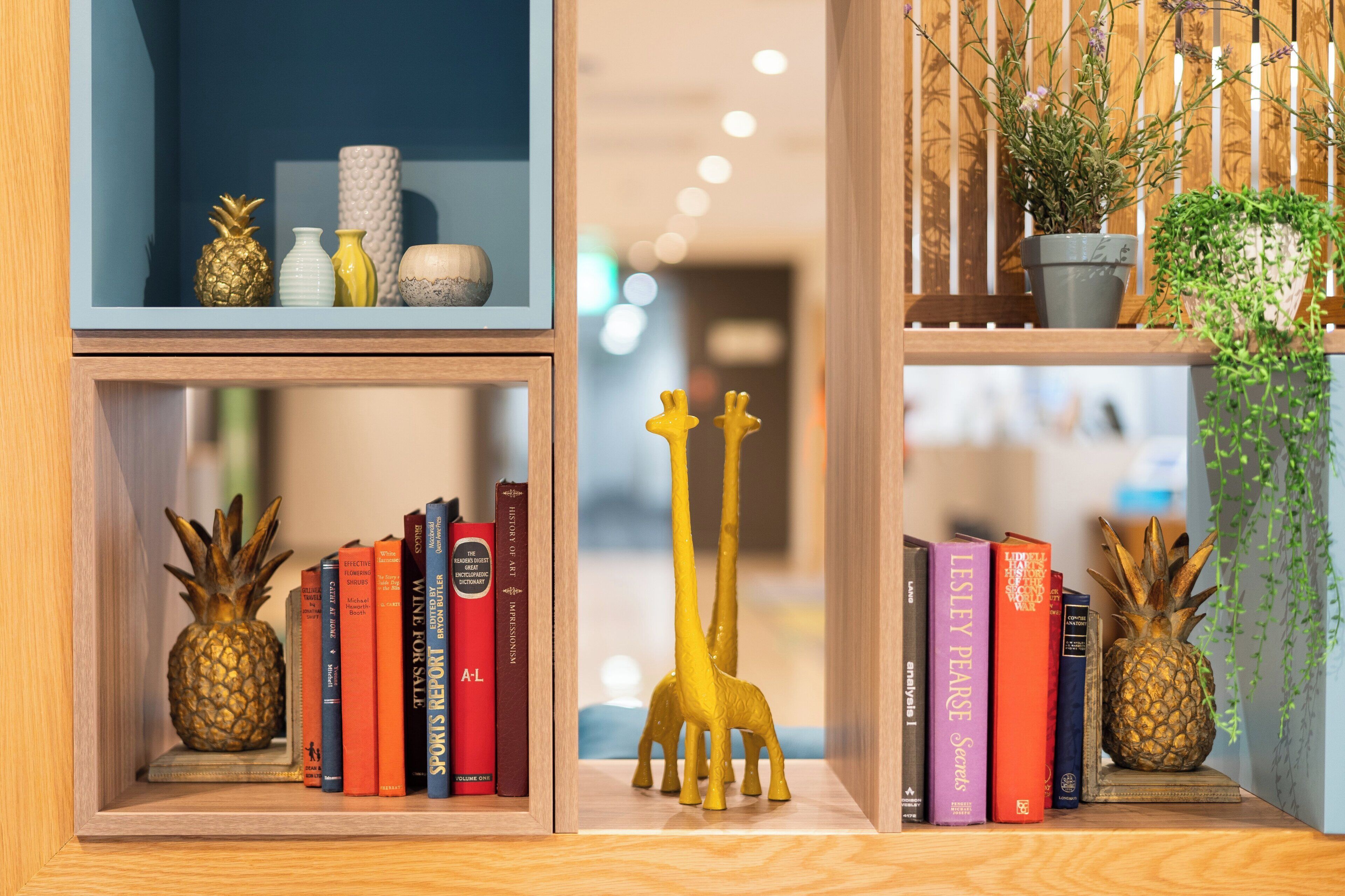 A bookshelf with books, a pineapple, and a giraffe figurine.