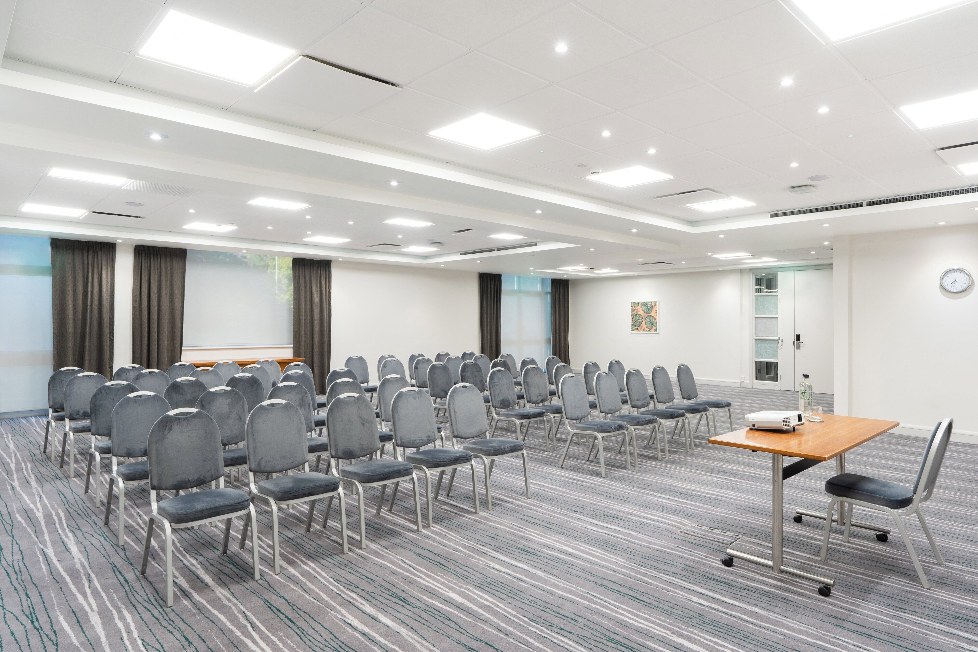 A conference room with rows of chairs, a projector, and a clock on the wall.