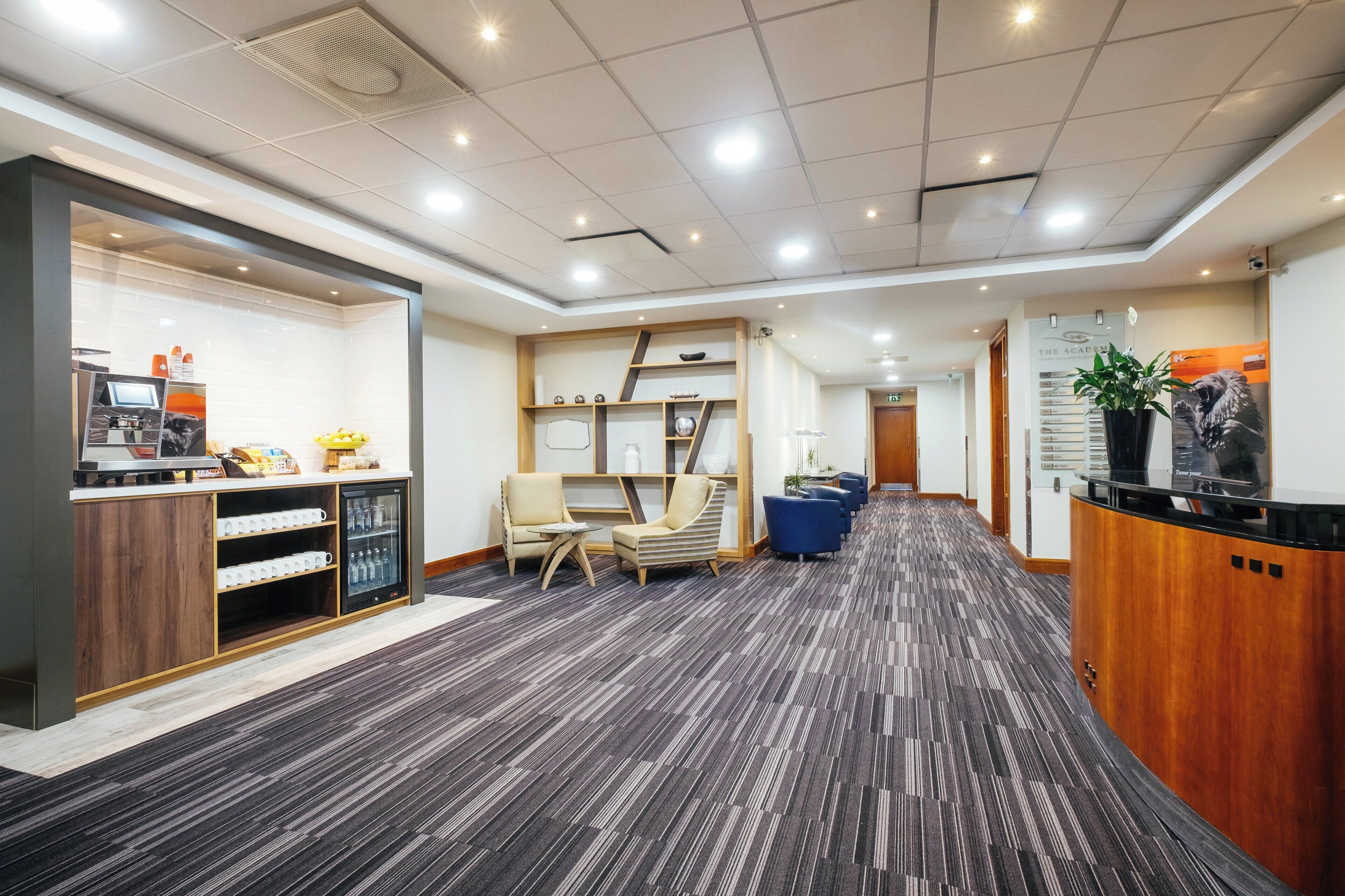 Zona de recepción de un hotel con mostrador, área de estar y una máquina de café.