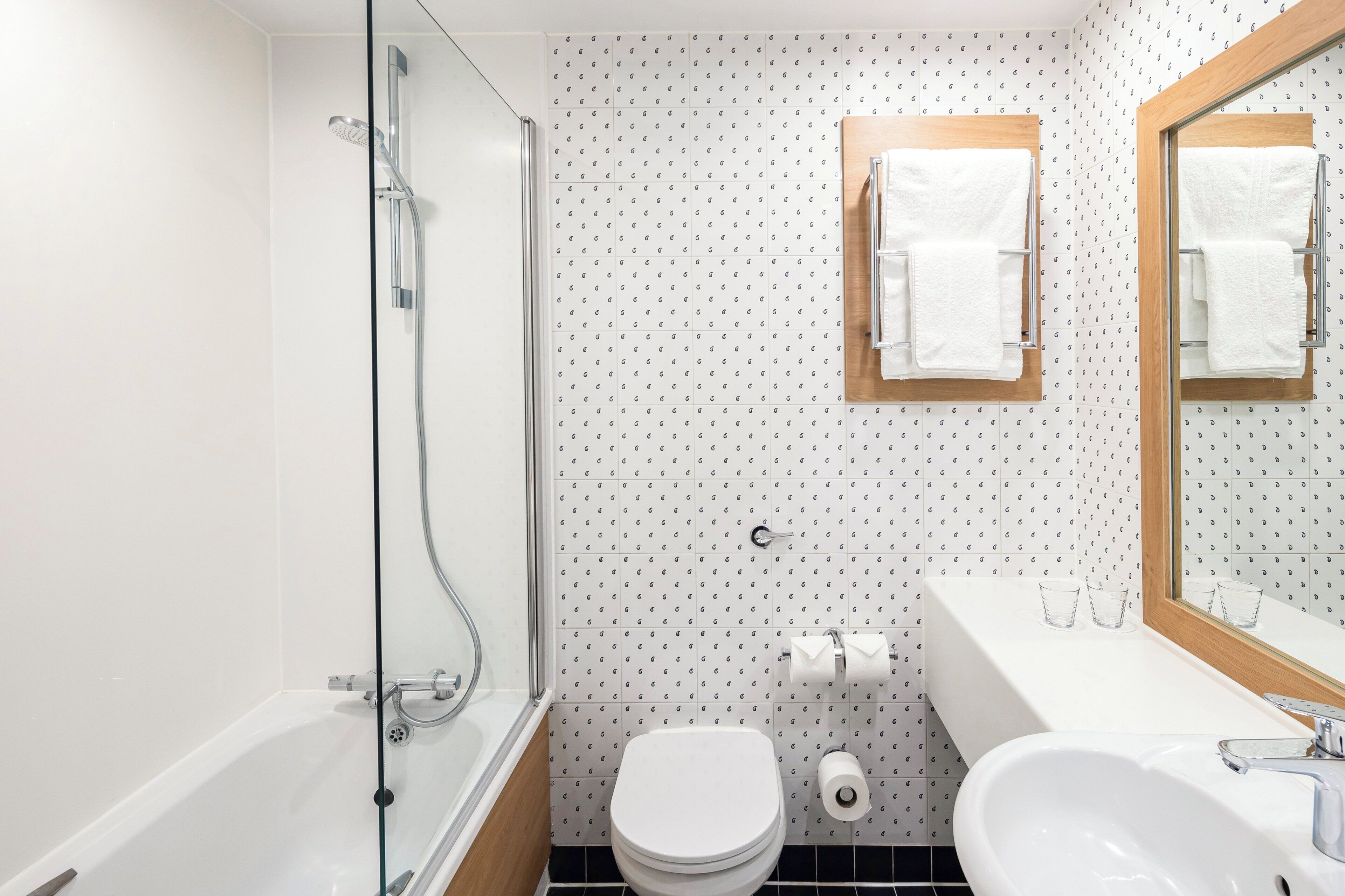 Un baño moderno con ducha envuelta en vidrio, inodoro blanco, lavabo con espejo y azulejos con diseño.