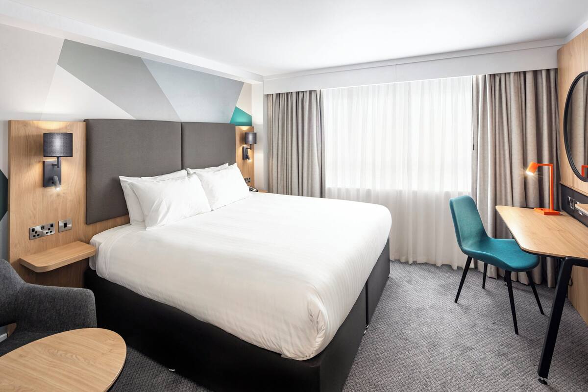 Une chambre d’hôtel moderne équipée d’un grand lit, d’un bureau, d’une chaise et d’un téléviseur.
