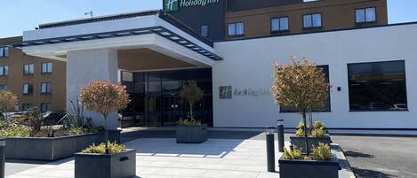 A Holiday Inn hotel with a modern design, featuring a covered entrance and potted plants.