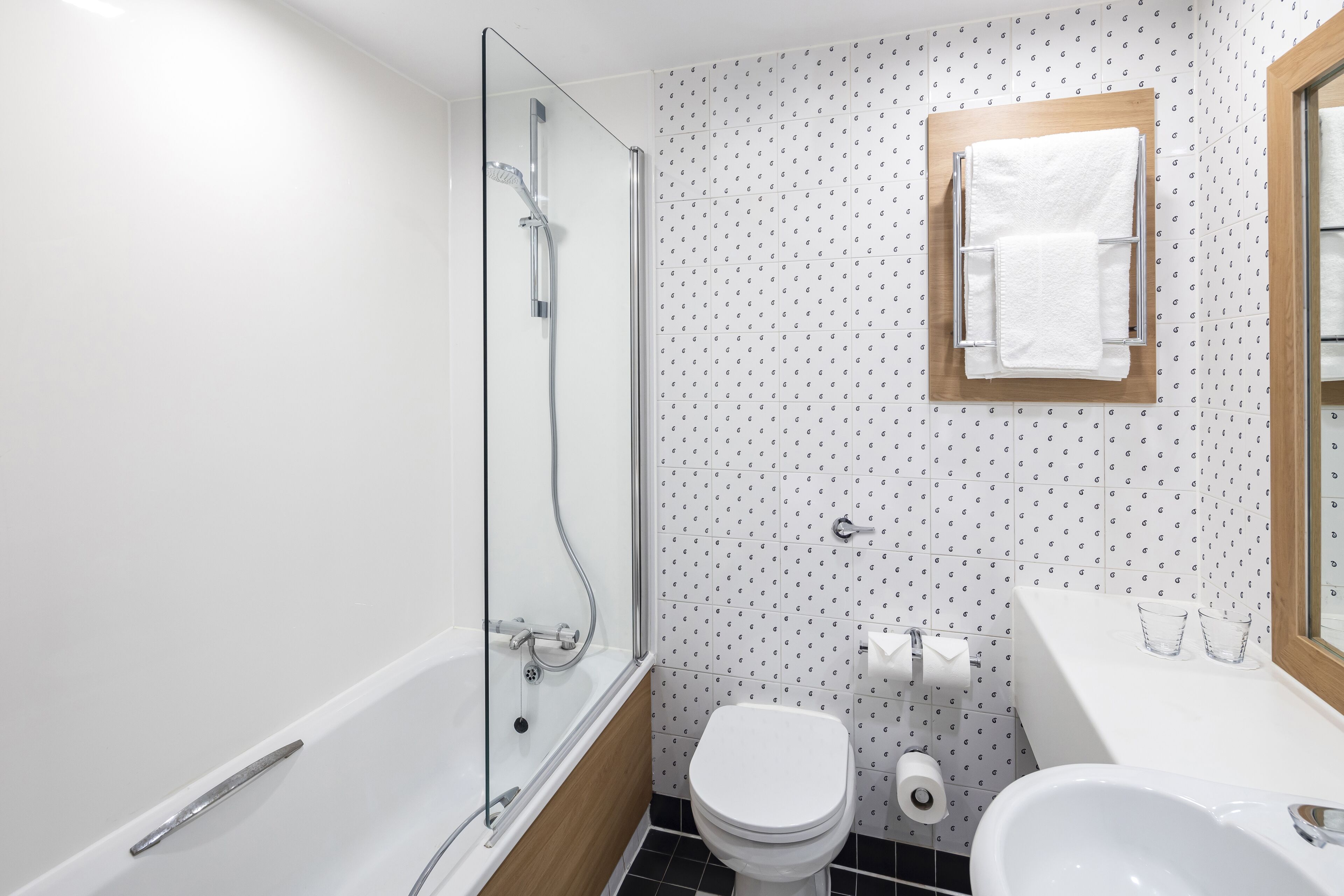 Un baño con ducha de mampara de vidrio, inodoro blanco y lavamanos con espejo.