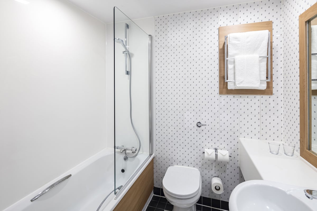 Un baño con ducha de mampara de vidrio, inodoro blanco y lavamanos con espejo.