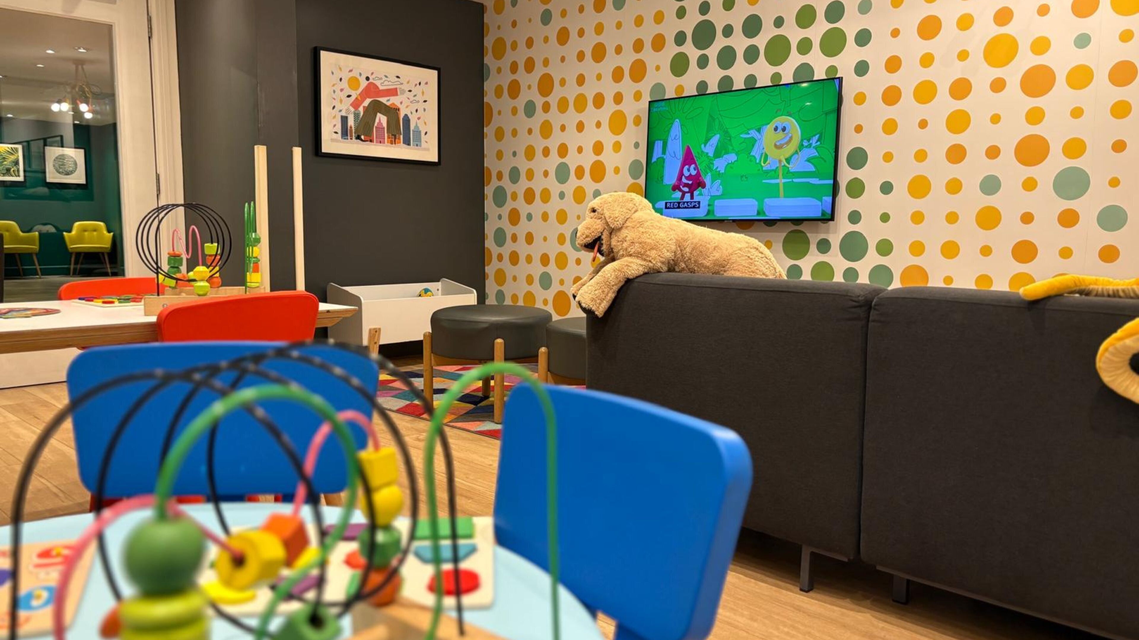 A children's play area with colorful toys, a sofa with a teddy bear, and a TV displaying a cartoon.