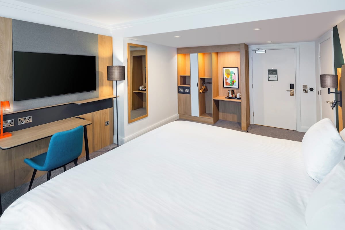Une chambre d’hôtel avec un grand lit, un bureau doté d’un téléviseur à écran plat, une chaise bleue, une armoire et une porte avec une pancarte.